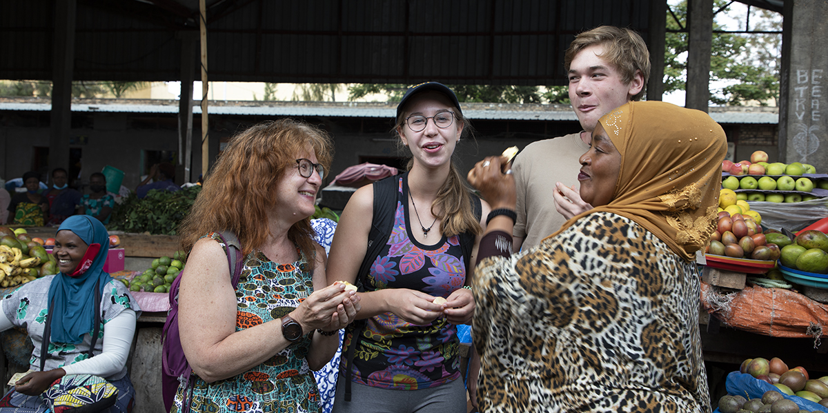 Visitors tasting fruit with a vendor at a Kigali market